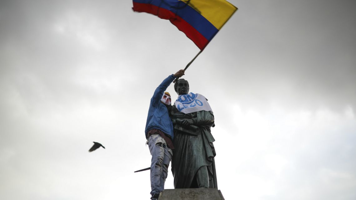 An anti-government demonstrator waves a Colombian flag after he climbed up to a statue of South American independence hero Simon Bolivar during a protest at Bolivar square in Bogota, Colombia