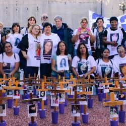 Family members of femicide victims stand behind their relatives crosses for a photo. 