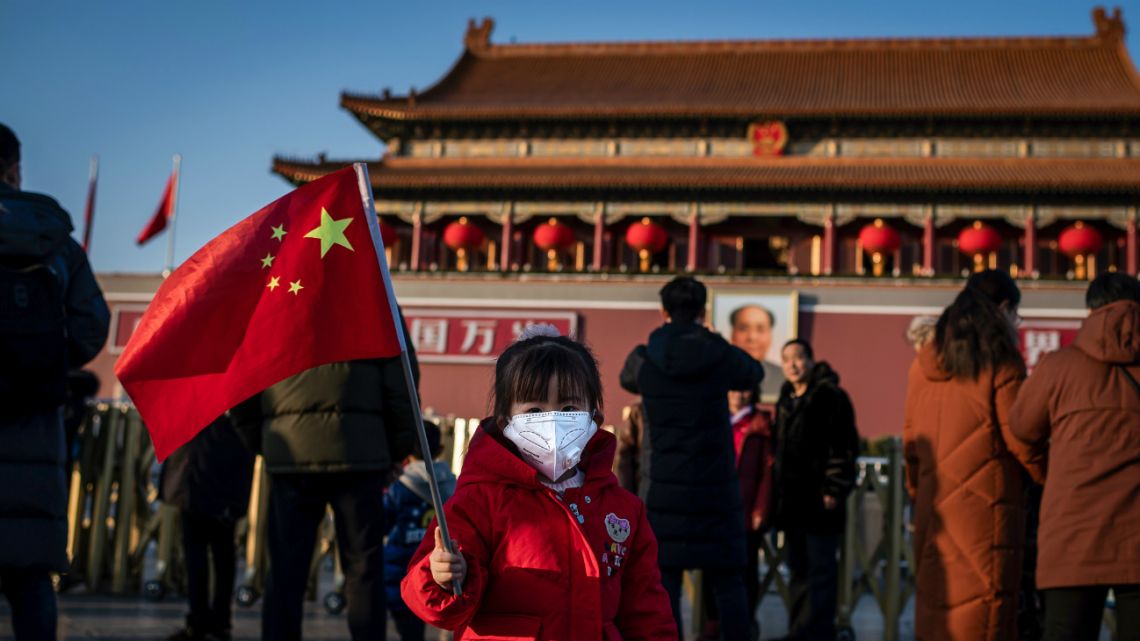 A young girl wearing a protective mask looks on as she waves a national flag in front of the portrait of late communist leader Mao Zedong (back) at Tiananmen Gate in Beijing on January 23, 2020