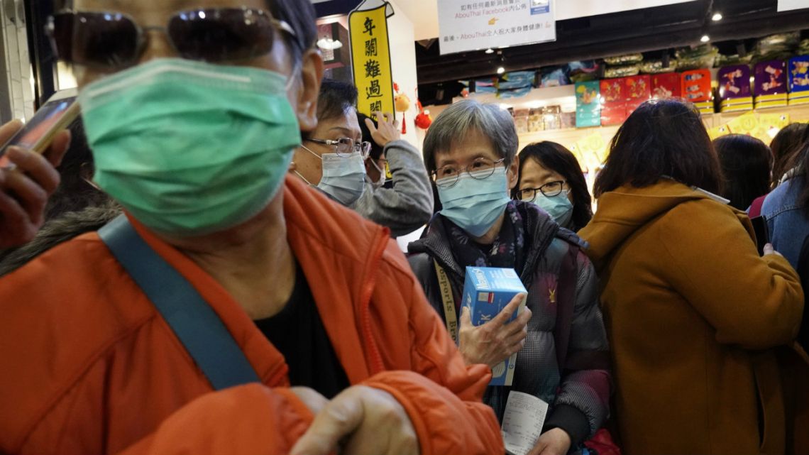 A woman holds a box of face mask as people queue up waiting to purchase face masks outside a shop in Hong Kong, which has reduced railroad service to Chinese mainland.
