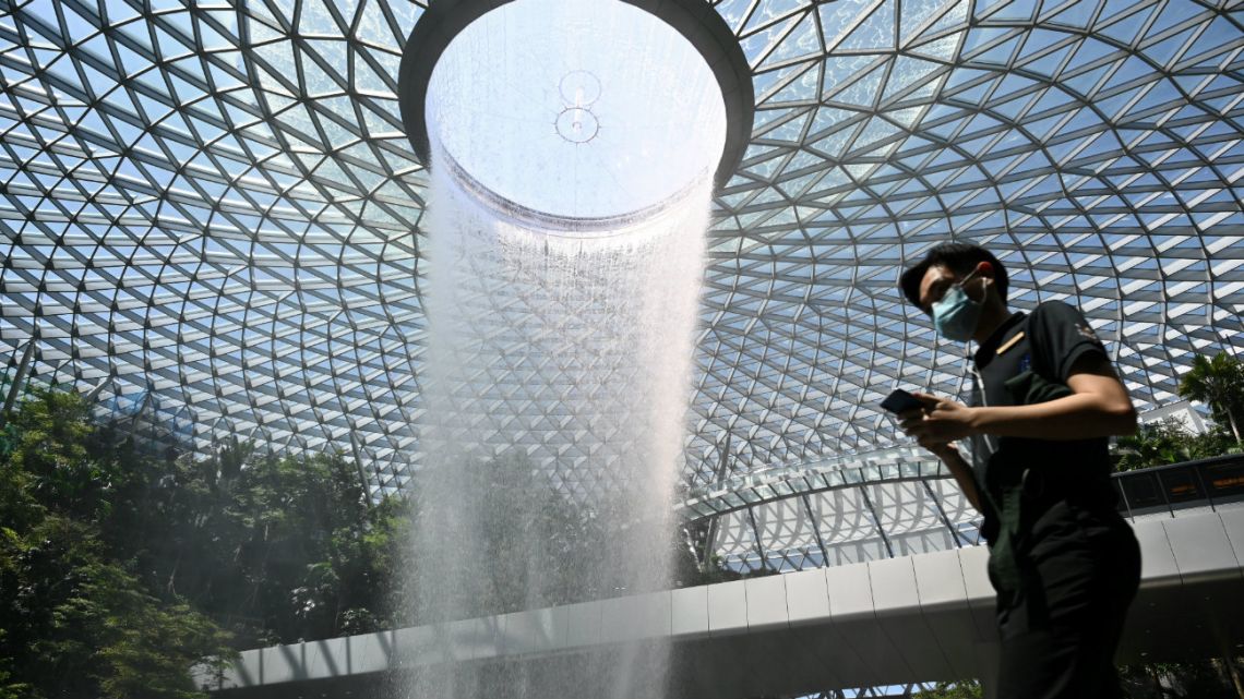 A man, wearing a protective facemask amid fears about the spread of the COVID-19 novel coronavirus, walks past the Rain Vortex display at Jewel Changi Airport in Singapore on February 27, 2020.