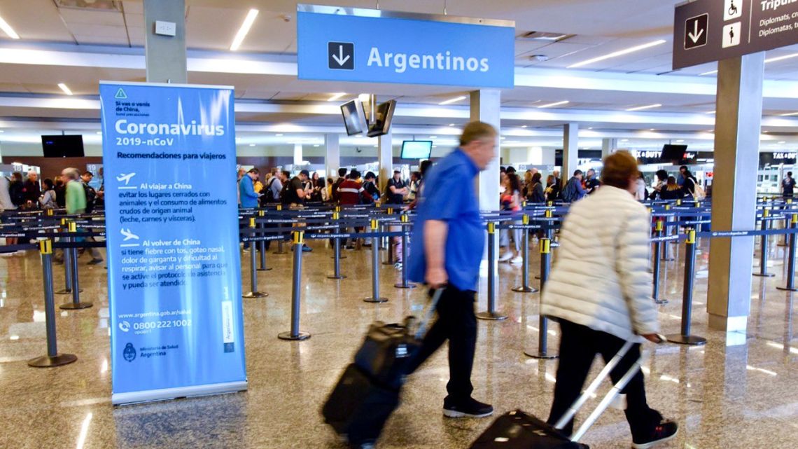 Passengers enter passport control at Ezeiza International Airport, with a sign informing them about precautions regarding the coronavirus outbreak.