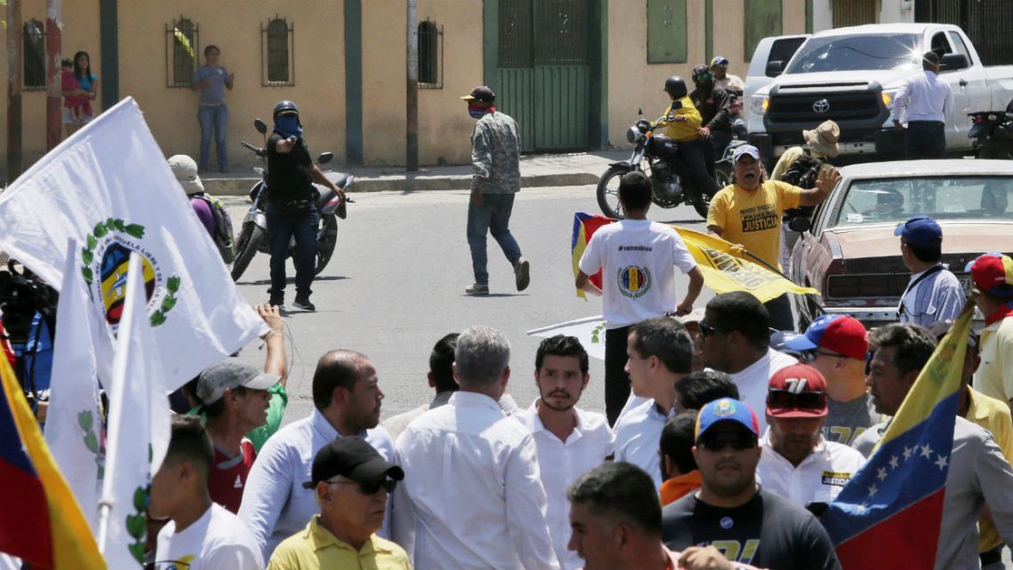 An unidentified man aims a gun at a crowd as opposition leader Juan Guaidó