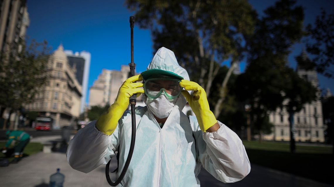 A worker adjusts his goggles as he sprays bleach at Plaza de Mayo in Buenos Aires Friday, March 20, 2020. 