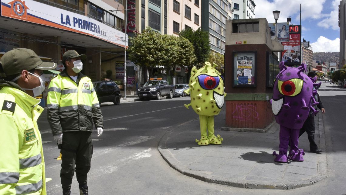 Bolivian police officers stand guard in the street next to two persons using costumes representing the shape of coronavirus, in La Paz on March 23, 2020.