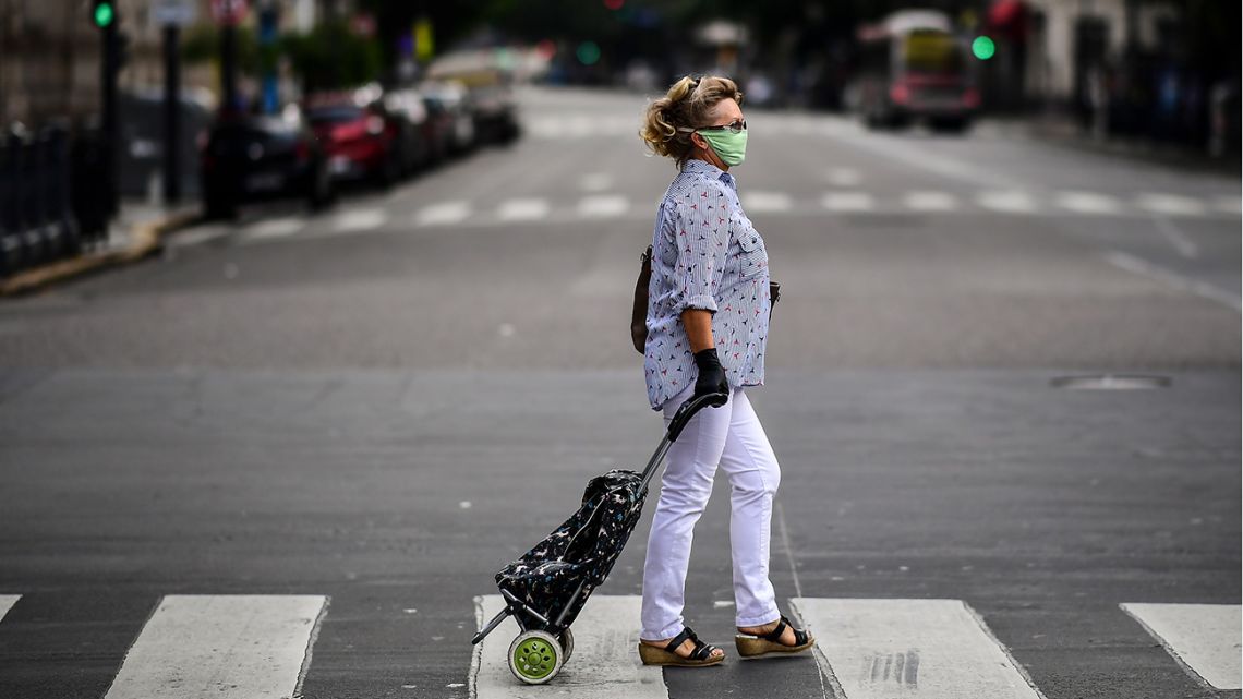 A woman wears a face mask and gloves against the spread of the new coronavirus as she crosses an empty Avenida Callao in Buenos Aires.