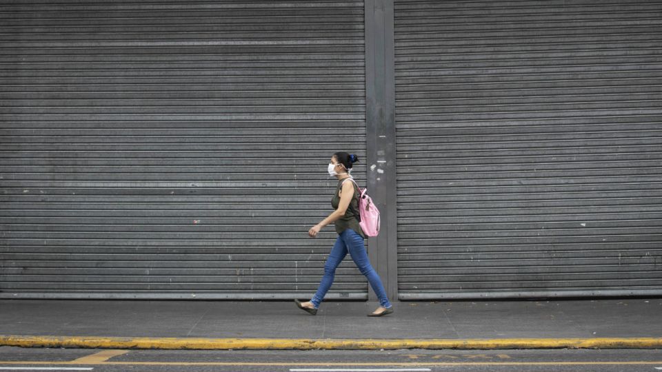 Una mujer porta una mascarilla mientras camina frente a un centro comercial cerrado durante la cuarentena obligatoria decretada por el gobierno, en la ciudad de Buenos Aires