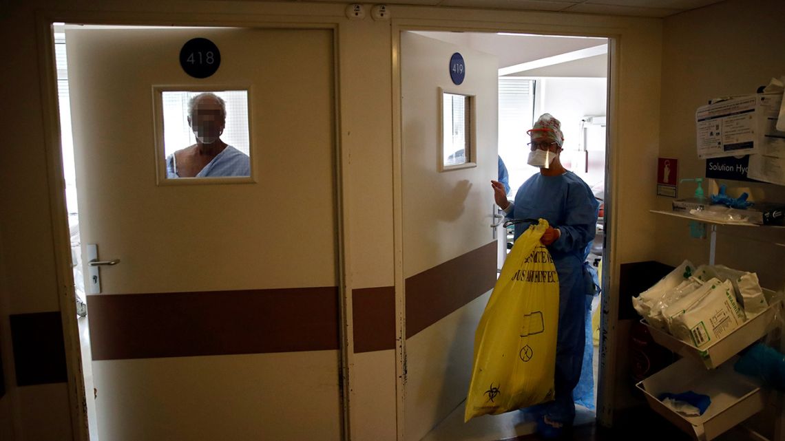 An infected man (left) looks out onto a corridor as a nurse leaves the room of a patient infected with Covid-19 at the intensive care unit of the Peupliers private hospital in Paris, on April 7, 2020.