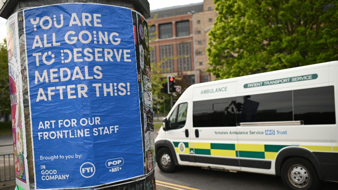 A poster pays tribute to staff in the front line in the fight against the COVID-19 illness as an ambulance passes by in Leeds, northern England, on April 23, 2020 as life continues under lockdown in Britain in an effort to halt the spread of the novel coronavirus.