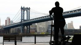 Solitaria, una personas ejercita este jueves 23 de abril en Nueva York, con el puente de Manhattan de fondo.