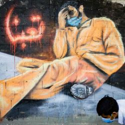 Un joven, con una máscara protectora, pasa junto a un mural que dice  | Foto:AFP