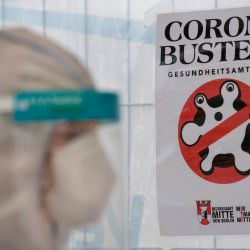 Berlín: un profesional de la salud con equipo de protección, careta y máscara facial se encuentra al lado de un cartel de  | Foto:AFP
