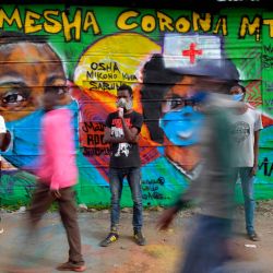 Los artistas de Grafitti de la Organización Juvenil Mathare Roots posan frente a su última mura abogando por prácticas de seguridad para frenar la propagación del nuevo coronavirus (Covid-19), mientras la gente pasa por el barrio marginal de Mathare, el 29 de abril de 2020, en la capital de Kenia, Nairobi. (Foto por TONY KARUMBA / AFP) | Foto:AFP