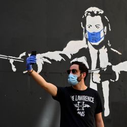 Un hombre se toma una foto selfie frente a una plantilla de graffiti que representa a los actores estadounidenses John Travolta y Samuel L. Jackson en sus papeles de  | Foto:AFP