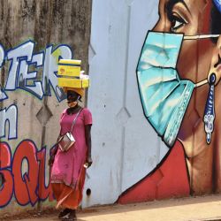 Una mujer camina más allá del graffiti en una pared que representa medidas de higiene para frenar la propagación del coronavirus COVID-19 en Conakry, Guinea, el 4 de mayo de 2020. (Foto de CELLOU BINANI / AF | Foto:AFP