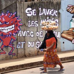 Una mujer camina junto al graffiti en una pared que representa medidas de higiene para frenar la propagación del coronavirus COVID-19 en Conakry, Guinea, el 4 de mayo de 2020. / AFP / CELLOU BINANI | Foto:AFP