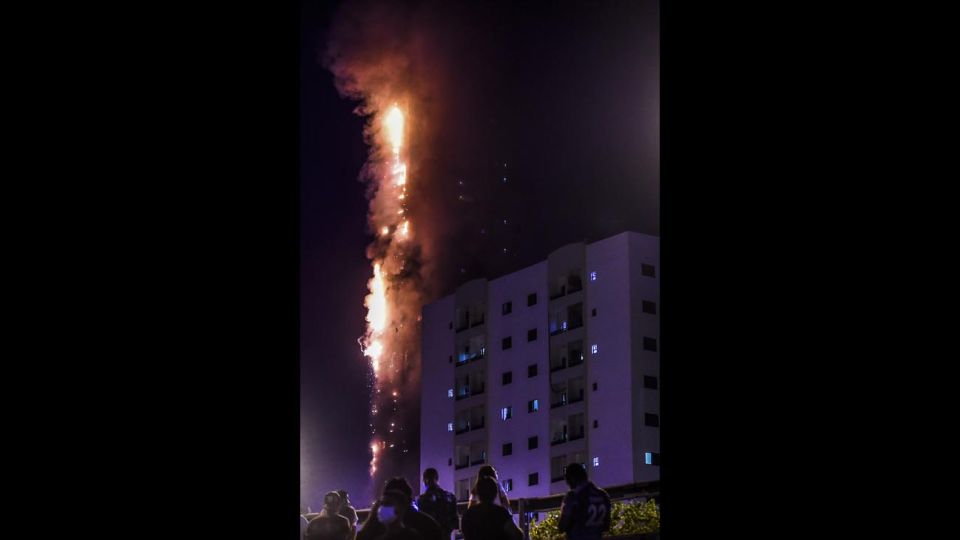 La gente se para en un puente y observa un incendio que se produce en una torre de 48 pisos en Sharjah, en los Emiratos Árabes.