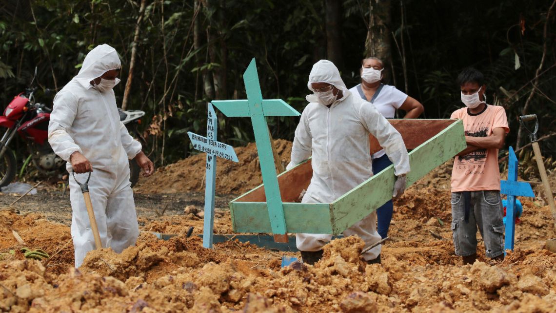 In this Thursday, April 16, 2020 photo, funeral workers in protective gear prepare a grave at the Nossa Senhora Aparecida cemetery, for a woman who is suspected to have died of COVID-19, in Manaus, Amazonas state, Brazil. 