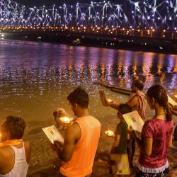 Un sacerdote hindú junto con devotos realizan el ritual 'Arti' (ondeando lámparas encendidas) en el sagrado río Ganges mientras el puente Howrah se ilumina con colores blancos para honrar a los 'guerreros de primera línea' del coronavirus COVID-19 en Kolkata el 9 de mayo. 2020. (Foto por Dibyangshu SARKAR / AFP) | Foto:AFP