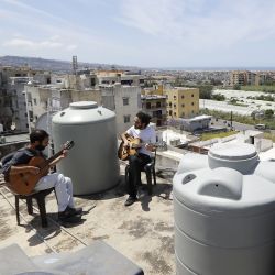 El músico libanés Ziad al-Zayyat (izq.) Y su compañero de piso, el diseñador de interiores Saad Molaeb, tocan sus guitarras en la azotea de su edificio, durante un bloqueo impuesto por las autoridades en un intento por detener la propagación del nuevo coronavirus en la ciudad de Hadath, al norte de la capital, Beirut, el 4 de mayo de 2020. - Por lo general, el reino de los tanques de agua y las antenas parabólicas, los techos de Líbano han sido recientemente agraciados por escenas improbables de residentes confinados que huyen de sus pisos por espacio y aire fresco. (Foto por JOSEPH EID / AFP) | Foto:AFP
