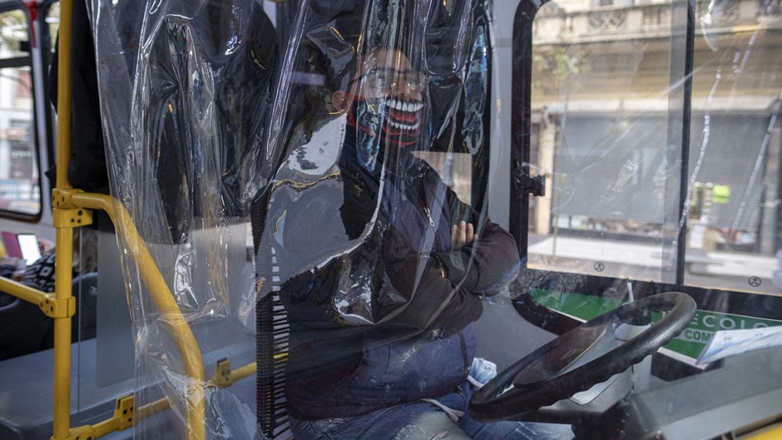 A bus driver wearing a protective mask sits behind a plastic screen in Buenos Aires.