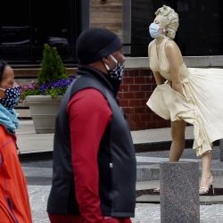 Las personas que usan mascarillas pasan junto a la estatua de Forever Marilyn de Seward Johnson, que también lleva una máscara en medio del brote de Coronavirus en National Harbor, Maryland, el 11 de mayo de 2020. (Foto de Olivier DOULIERY / AFP) | Foto:AFP