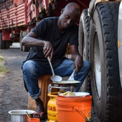 Una foto tomada el 5 de mayo de 2020 muestra a un conductor de camión preparando un Iftar, la cena que los musulmanes terminan con su ayuno diario en el Ramadán, junto a su camión, ya que ha estado esperando durante cinco días para que le hagan la prueba del coronavirus COVID-19 antes de ingresar. a Kenia como obligatorio para todos los conductores en Namanga, norte de Tanzania. (Foto por Filbert RWEYEMAMU / AFP) | Foto:AFP