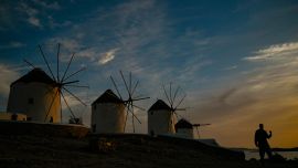 Un hombre camina por los antiguos molinos en la isla griega de Mykonos, en las Cícladas, el 12 de mayo de 2020. - En Mykonos, al comienzo de la temporada turística, la imagen es sorprendente: la elegante isla tradicionalmente llena de extranjeros adinerados se ha convertido en un isla fantasma, que ofrece a los visitantes callejones desiertos, tiendas cerradas, restaurantes y hoteles abandonados. (Foto por ARIS MESSINIS / AFP)