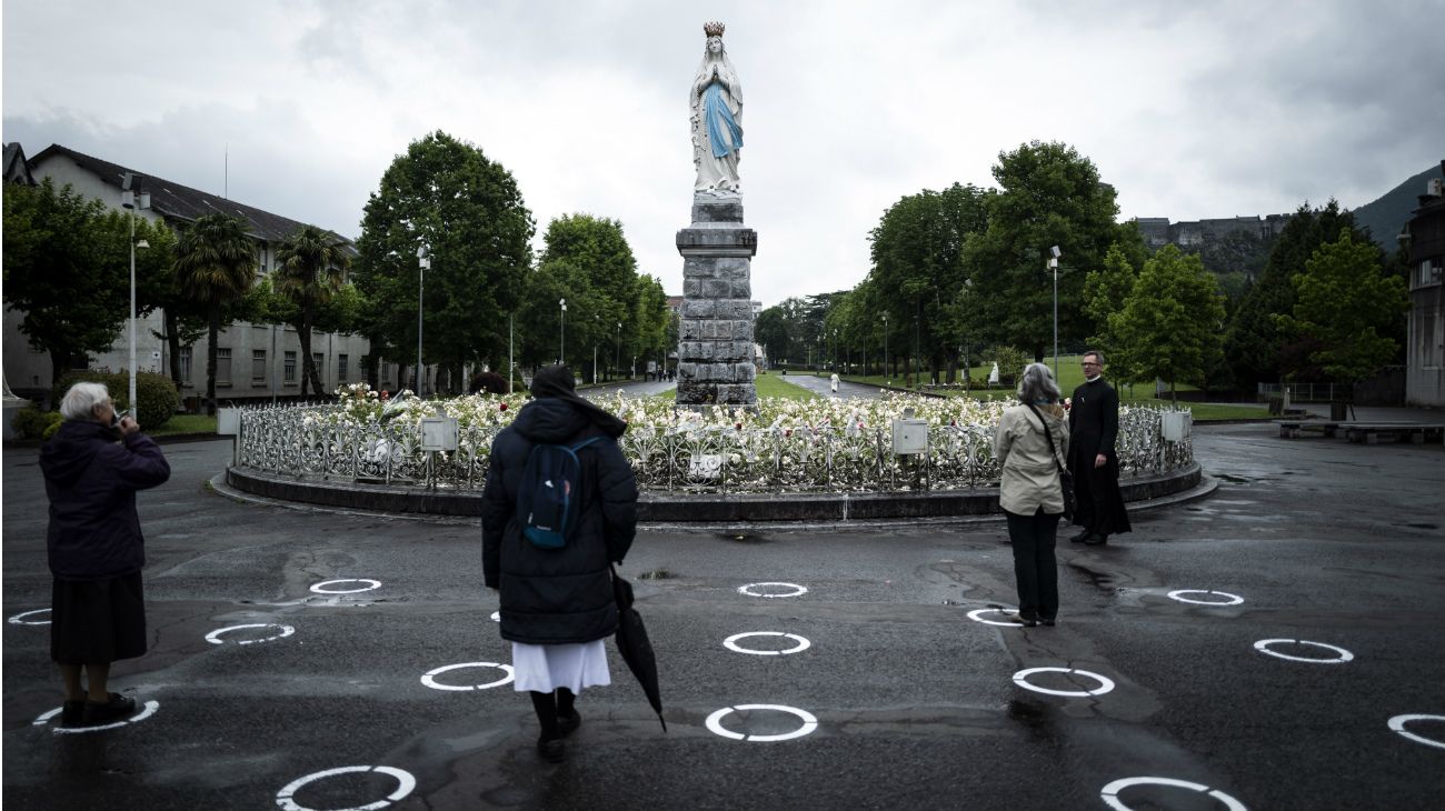 Ciudadanos en carteles de distanciamiento frente a la estatua de La vierge couronnee en el Santuario de Nuestra Señora de Lourdes en Lourdes, suroeste de Francia