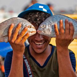 Un joven posa mientras sostiene dos peces frente a él en la ciudad portuaria de Faw, en el sur de Irak, a 90 kilómetros al sur de Basora, cerca de Shatt al-Arab y el Golfo, el 18 de mayo de 2020. - En Irak, un bloqueo nacional para detener La pandemia del coronavirus COVID-19 ha encontrado algunos admiradores inesperados: empresas locales que ya no tienen que competir con las importaciones turcas, iraníes o chinas. Esos países, así como Arabia Saudita, Jordania y Kuwait, suelen inundar los mercados iraquíes con productos económicos a precios con los que los productores locales no pueden competir. (Foto por Hussein FALEH / AFP) | Foto:AFP