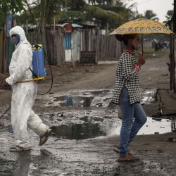 Una mujer se protege de la lluvia cuando un funcionario del Ministerio de Salud rocía desinfectante en Toamasina, una importante ciudad portuaria en la costa este de Madagascar. | Foto:RIJASOLO / AFP