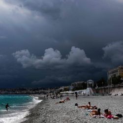 La gente yacía en una playa bajo nubes oscuras cerca de la  | Foto:VALERY HACHE / AFP