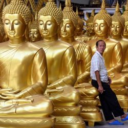 Un empleado se apoya en una estatua de Buda en una tienda que vende figuras religiosas budistas en Bangkok. | Foto:Mladen Antonov / AFP