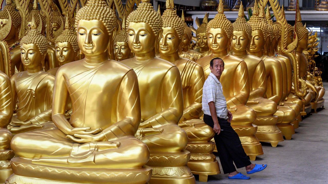 Un empleado se apoya en una estatua de Buda en una tienda que vende figuras religiosas budistas en Bangkok. | Foto:Mladen Antonov / AFP