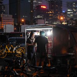 La gente compra comida de un vendedor ambulante cerca de una salida de metro en Beijing. | Foto:GREG BAKER / AFP