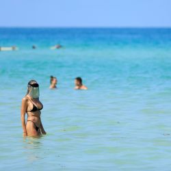 Una mujer usa un protector facial mientras camina en el océano frente a South Beach en Miami Beach, Florida.  | Foto:Cliff Hawkins / Getty Images / AFP
