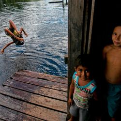 Un niño salta al río Quaqualino junto a otros mirando a la cámara, en la comunidad de Sao José, a una hora y media de Megalco, en el suroeste de la isla de Marajo, estado de Pará, Brasil. | Foto:TARSO SARRAF / AFP