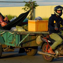 Un hombre monta una moto tirando de un remolque con una mujer descansando en una hamaca, revisando su teléfono, en una calle de Phnom Penh. | Foto:TANG CHHIN SOTHY / AFP