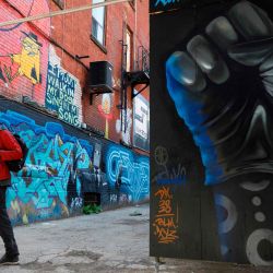 Un hombre pasa junto a un puño enguantado pintado en una pared en Graffiti Alley en Toronto, Ontario, Canadá. - El famoso callejón de Toronto está siendo pintado con prominentes figuras negras y mensajes de solidaridad contra el racismo anti-negro en apoyo. del movimiento Black Lives Matter.  | Foto:Cole Burston / AFP