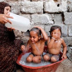 Una madre palestina baña a sus hijos en medio de una ola de calor durante la actual crisis pandémica de coronavirus Covid-19 en la ciudad de Gaza. | Foto:MOHAMMED ABED / AFP