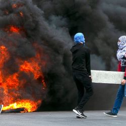 Los manifestantes palestinos llevan un bloque de cemento y queman llantas mientras chocan con las tropas israelíes durante una protesta contra el plan de Israel de anexar partes de la Cisjordania ocupada, cerca de la ciudad de Ramallah. | Foto:ABBAS MOMANI / AFP