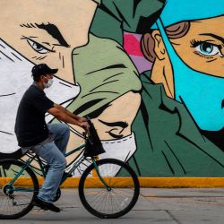 Un hombre viaja en bicicleta frente a un mural relacionado con el coronavirus de los artistas urbanos Mick Martínez y  | Foto:HERIKA MARTINEZ / AFP