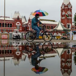 Un ciclista con un paraguas circula junto a un charco de agua después de la lluvia en Chennai. | Foto:Arun Sankar / AFP
