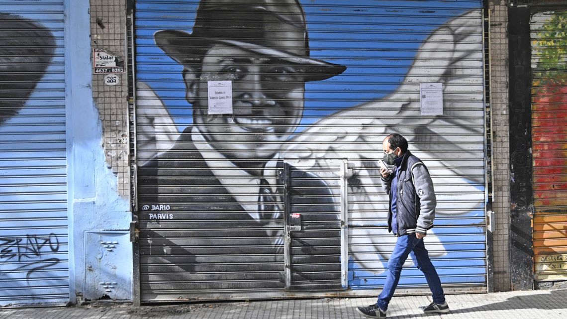 A man passes by a closed store with a portrait of tango singer Carlos Gardel.