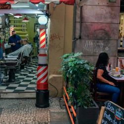 Un hombre se corta el cabello mientras la gente almuerza en un restaurante en Sao Paulo, Brasil, cuando los bares, restaurantes y salones de belleza de la ciudad reabrieron sus puertas después de más de tres meses de encierro para luchar contra el COVID. 19 pandemia de coronavirus. | Foto:NELSON ALMEIDA / AFP