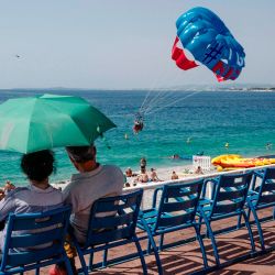 La gente se sienta a lo largo de la Promenade des Anglais viendo parasailing en la ciudad de Niza. | Foto:VALERY HACHE / AFP