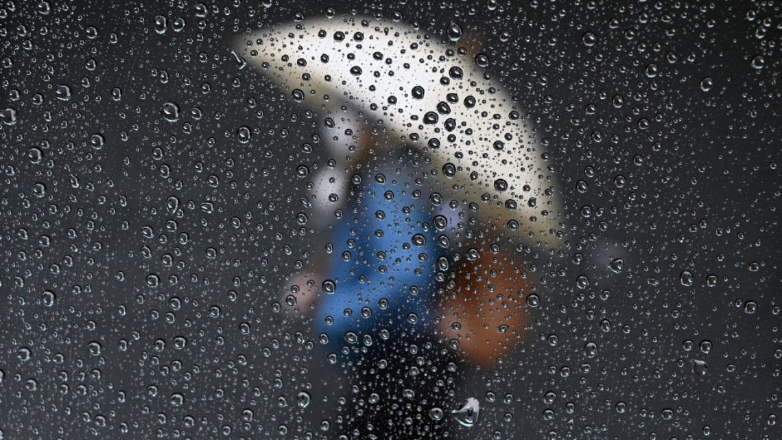 Raindrops are seen on a taxi window while a woman passes by a closed store in Buenos Aires on June 30, 2020.