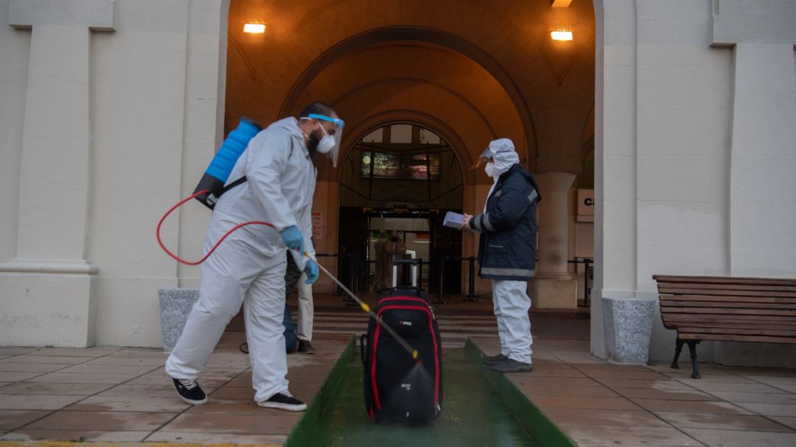 An employee in protective suit disinfects a passenger's piece of luggage outside Argentinian ferry service company Buquebus' terminal in the port of Montevideo, on July 10, 2020, amid the new coronavirus pandemic. 