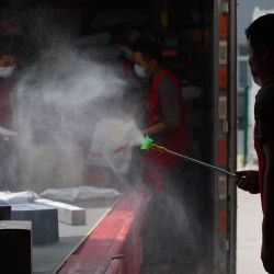 Un trabajador desinfecta los paquetes cuando se descargan de un camión en un centro de distribución de JD.com en Beijing. | Foto:GREG BAKER / AFP