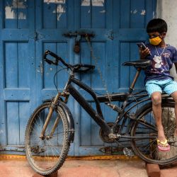 Un joven con una máscara facial se sienta frente a una tienda cerrada mientras usa un teléfono móvil después de que las tiendas cerraron como medida preventiva contra el coronavirus COVID-19 en Hyderabad. | Foto:NOAH SEELAM / AFP
